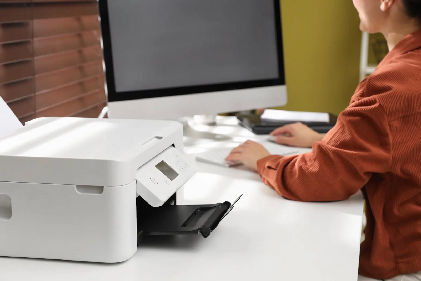 Office printer on a desk with a woman working at her computer