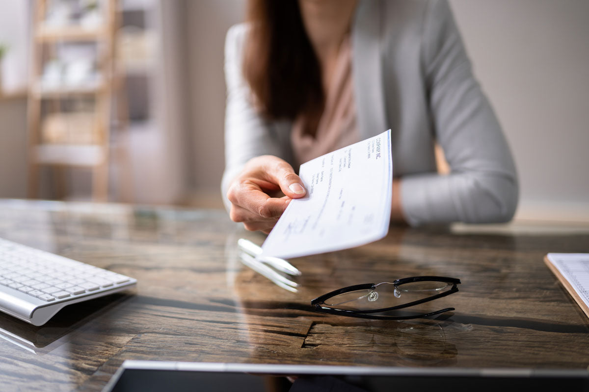 First person view of a business women handing a business check across her desk.