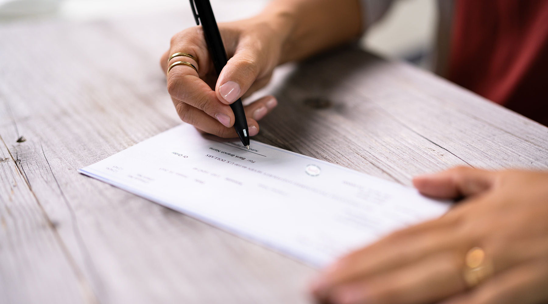 Person signing Check Depot business check on white wooden desk with black pen