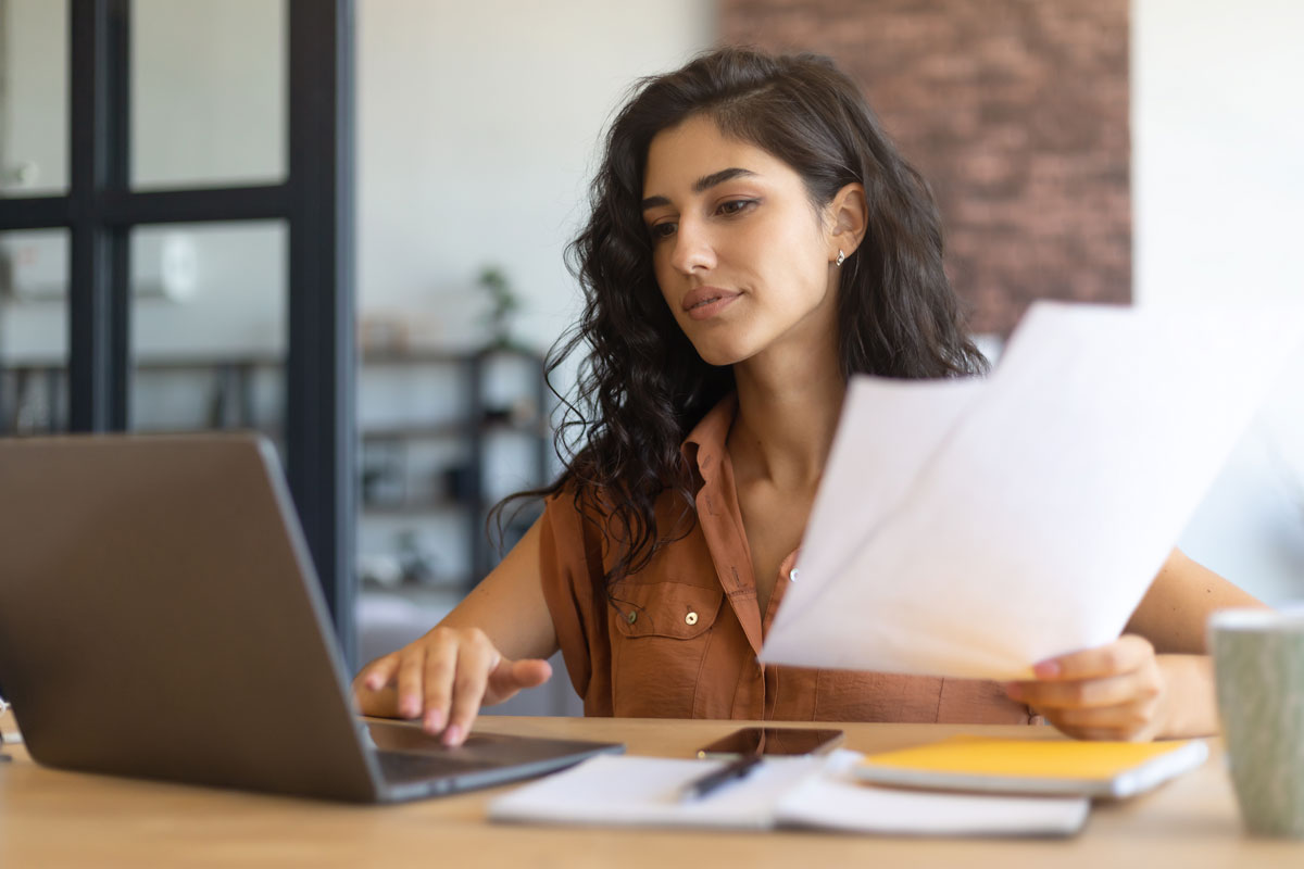 Women working in an office on a laptop while holding business check paper in her free hand.