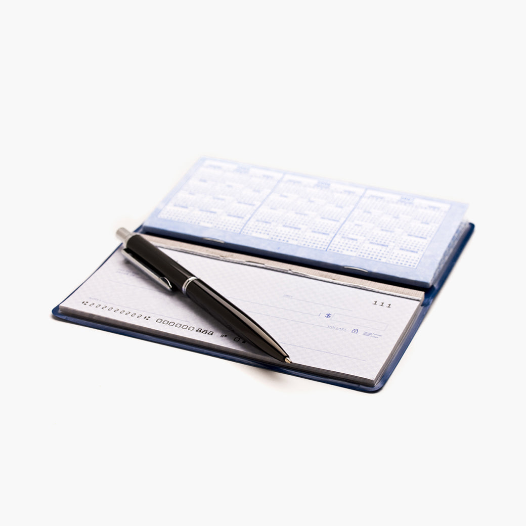 a personal checkbook opened displaying checks and a register with a black pen laid across it